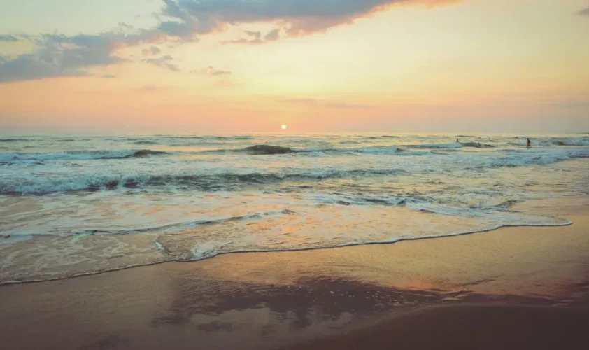 A beach sunset displays soft colours and gentle waves, with a distant horizon creating a serene and calming scene.