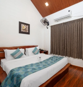 King-size bed with teal accent pillows and wooden flooring in Tree House Suite bedroom at Orchid Hotel Panchgani