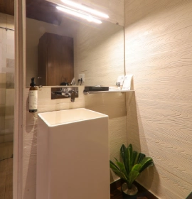 Modern bathroom with white vessel sink, beige textured tiles and glass shower in Wooden Cottage Suite Panchgani