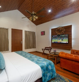 Wooden Cottage Suite bedroom with large smart TV, leather sofa and wooden ceiling fan at Orchid Hotel Panchgani