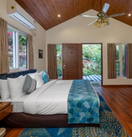 King-size bedroom with teal accents, ceiling fan and lush garden view in Wooden Cottage Suite at Orchid Hotel Panchgani