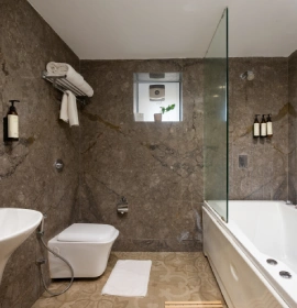 Strawberry Club Room luxury bathroom with marble walls, bathtub, glass shower partition and wall-hung toilet at Orchid Hotel Panchgani