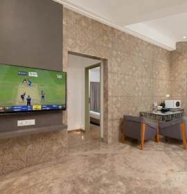 Strawberry Club Room interior with wall-mounted smart TV, textured stone wall and kitchenette counter at Orchid Hotel Panchgani