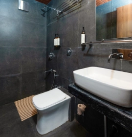 Modern bathroom with dark marble tiles, rainfall shower and vessel sink in Tree House Suite Panchgani