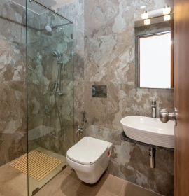 Wooden Tree House bathroom with marble tiles, glass shower enclosure, toilet and wall-mounted basin in Panchgani