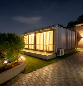 Wooden Tree House illuminated exterior with glass windows, AC unit and garden at night in Panchgani